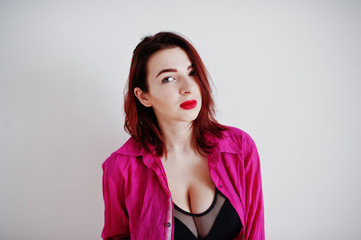Fototapeta premium Red haired girl with a big bust on black bra and rose shirt against white wall at empty room.