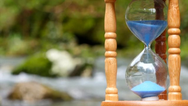 Hourglass on the background of a mountain river