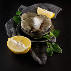 fresh raw king prawns with lemon and lemon balm on dark slate kitchen plate with napkin can be used as background