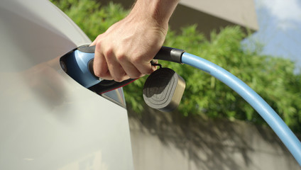 CLOSE UP: Young man recharging luxury white Tesla electric car at home © helivideo