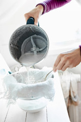 woman preparing vegan almond or coconut milk at home. Pouring the milk into a cheese cloth to...