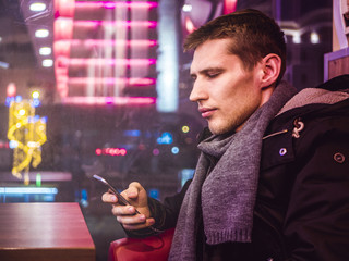 young man sitting at the table near the window with the smartphone