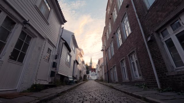 Walking in typical European street on paving stones, along small and big well-groomed houses, benches. Good weather at sunset. Cozy streets of villages in Norway. Lifestyle in suburbs and small towns.