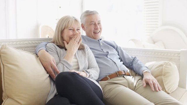 Mature relaxed couple watching and reacting to something on television