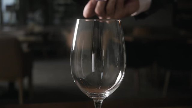Bartender pours red wine in glass from big transparent vessel