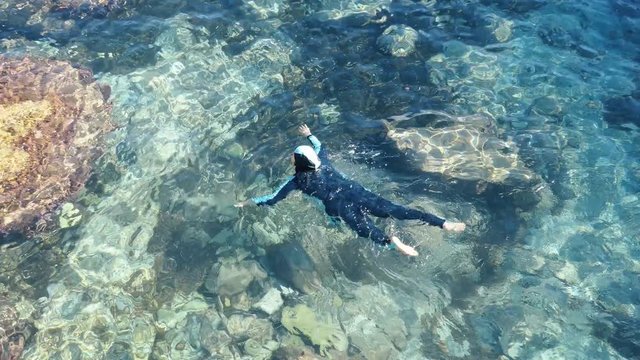 A Muslim woman is swimming in a turquoise sea. Europe.