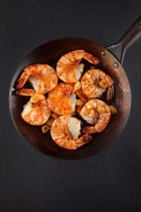 fresh prepared king prawns in an iron pan with garlic on dark slate kitchen plate can be used as background