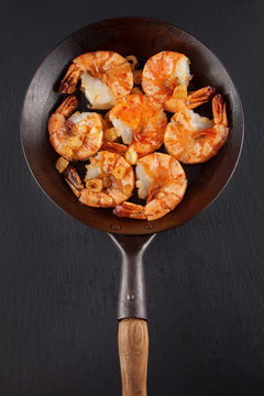 fresh prepared king prawns in an iron pan with garlic on dark slate kitchen plate can be used as background