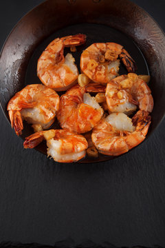 fresh prepared king prawns in an iron pan with garlic on dark slate kitchen plate can be used as background