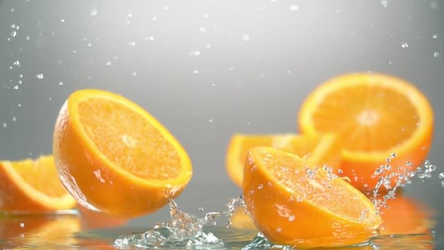 Orange hits orange juice surface and splits into halves. Slow motion shot