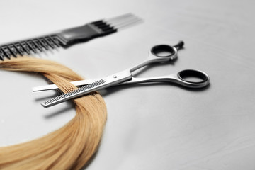 Professional hairdresser scissors, comb and strand of blonde hair on grey background