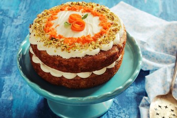 Homemade Carrot Cake with cream cheese frosting nuts toppingon blue wooden background