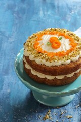 Homemade Carrot Cake with cream cheese frosting nuts toppingon blue wooden background