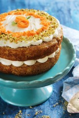 Homemade Carrot Cake with cream cheese frosting nuts toppingon blue wooden background