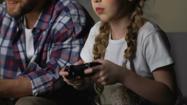 Little girl pressing joystick buttons playing video game with father at home