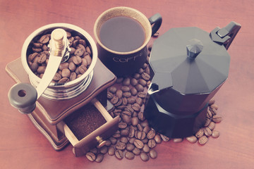 Manual coffee grinder with roasted  coffee beans, cup of coffee and moka pot on wooden table 