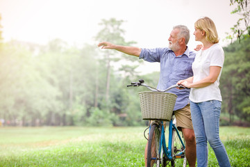 Senior old men couple walking their bike along happily talking happily.