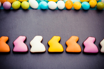 Easter colorful sweet rabbits in a row with small eggs on slate board. Top view. Copyspace