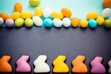 Happy Easter. Colorful chocolate rabbits in a row with small eggs on slate board. Top view. Copyspace