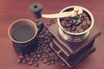 Roasted coffee beans, vintage manual coffee grinder and cup of coffee on wooden table, top view