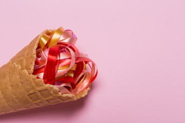 ice cream cone and colored ribbons on a pink background, copy space