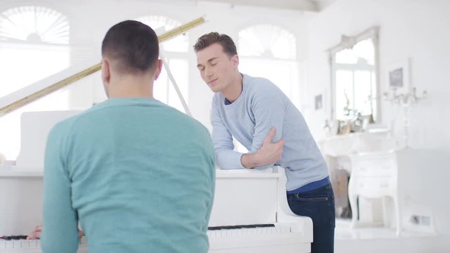Handsome male listens to his partner play the piano in their beautiful apartment