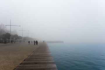 People walking on the waterfront of Thessaloniki, Greece, on a foggy day