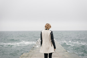 The girl stands with her back on the pier and looks at the sea.