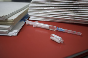 syringe with an open ampoule on a red notebook on a metal medical table