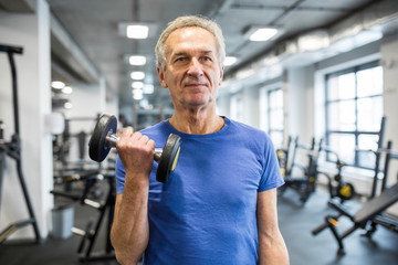 Fototapeta na wymiar Strong senior man holding dumbbell in gym
