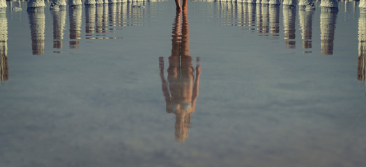  A beautiful, sporty, feminine girl walks along the water, reflecting her reflection.