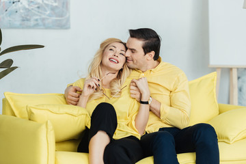 Embracing man and woman sitting on yellow sofa