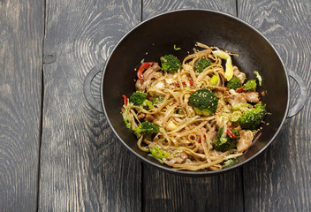 The food in the wok - noodles with meat and vegetables, on wooden surface