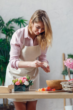 Portrait of young blonde florist composing bouquet of marshmallows, flowers