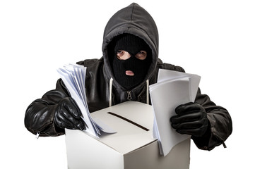 Election fraud and vote rigging concept with a thief wearing a hoodie, ski mask and leather gloves is ballot stuffing an electoral voting box, isolated on white with a clipping path cutout