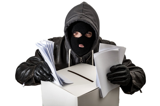 Election Fraud And Vote Rigging Concept With A Thief Wearing A Hoodie, Ski Mask And Leather Gloves Is Ballot Stuffing An Electoral Voting Box, Isolated On White With A Clipping Path Cutout