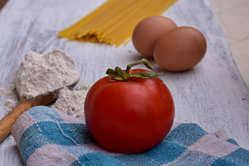 Raw homemade pasta with flour, eggs and tomato on rustic background. Uncooked spaghetti/ Kitchen- food background