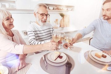 Happy to meet together. Positive delighted elderly couple sitting at the table and drinking wine while meeting with their adult son