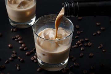Verser la crème irlandaise dans un verre avec de la glace, entouré de grains de café sur fond noir foncé