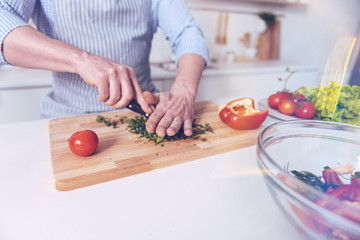 Healthy nutrition. Pleasant man holding knife and cooking while cutting vegetables for salad