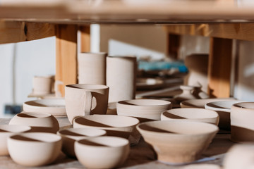 ceramic cups and bowls on wooden shelves in pottery workshop