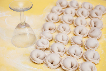 Fototapeta na wymiar Untreated only molded dumplings lie in rows on a yellow silicone board diagonally next to an inverted glass