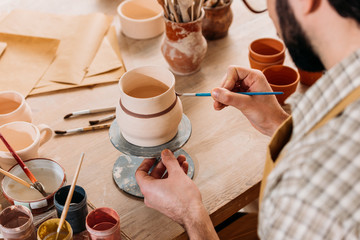 cropped view of potter painting ceramic jug in workshop