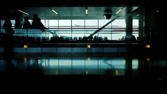 Silhouettes of people in the airport terminal. They hurry on their flight and on business. Outside the window you can see a flying airplane
