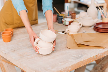 cropped view of female potter with ceramic dishware