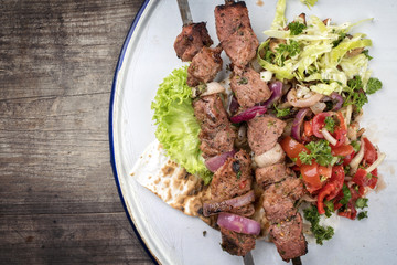 Traditional Greek souvlaki barbecue skewer with cabbage and tomato onion salad as top view on phyllo bread with copy space left