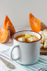 Delicate vegetable cream soup with pumpkin and croutons and slices of pumpkin on a light background.
