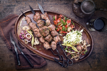 Traditional Turkish lamb kebab barbecue skewer with cabbage and tomato onion salad as top view on a plate - vintage