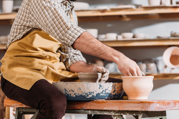 cropped view of potter making ceramic pots on pottery wheel in workshop