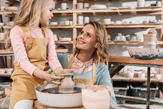 Female Teacher And Child Making Ceramic Pot On Pottery Wheel In Workshop